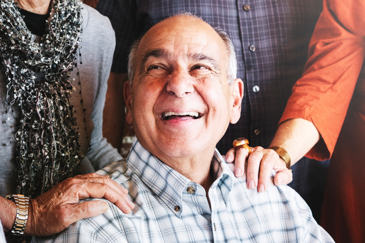 senior man with loved ones hands on his shoulders